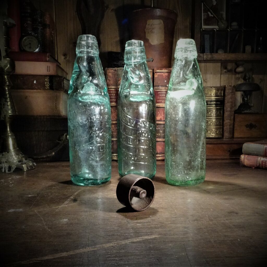 Three codd bottles with a codd bottle opener or codds wallop laying in the front.